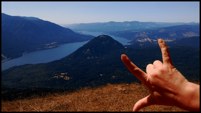 Hand giving the I Love You sign on top of a mountain overlooking the Washington gorge on a sunny day